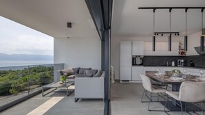 A modern apartment with a balcony overlooking a scenic view, a dining area with a table set for four, and a kitchen with dark countertops and white cabinets. - 3 bedroom cozy apartment in Kostrena (Kostrena)