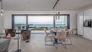 A modern dining area with a large window overlooking a scenic view, contemporary furniture, and a minimalist kitchen. - 3 bedroom cozy apartment in Kostrena (Kostrena)