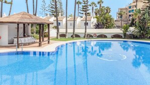 Una piscina azul cristalina con un puesto de salvavidas, una zona de estar cubierta y una fila de palmeras.