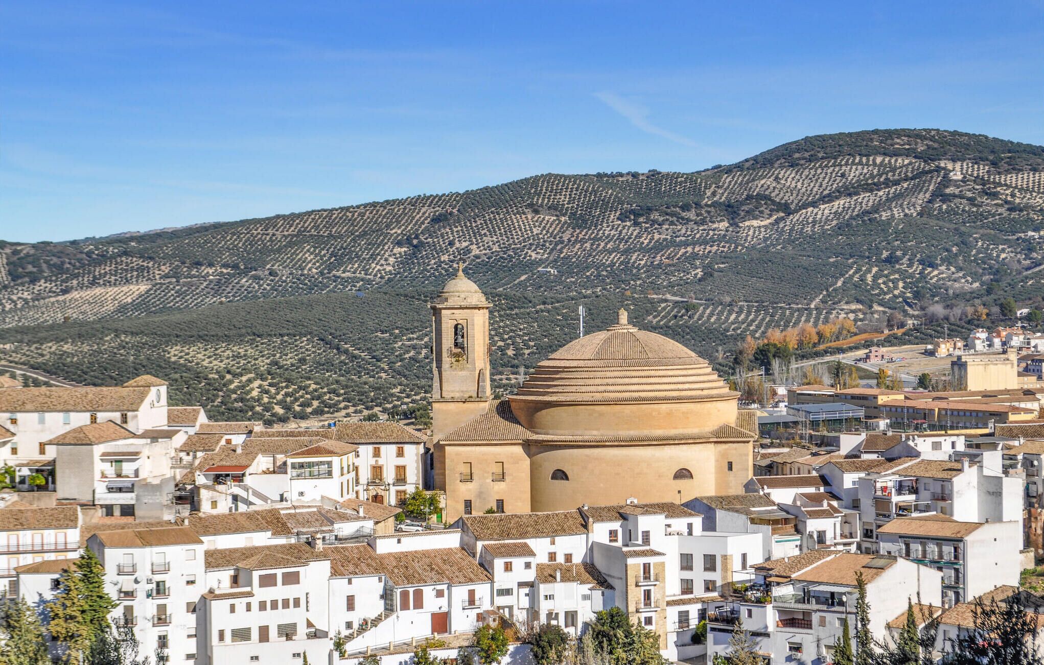 A town with a prominent church featuring a bell tower and a dome, surrounded by white buildings with terracotta roofs.