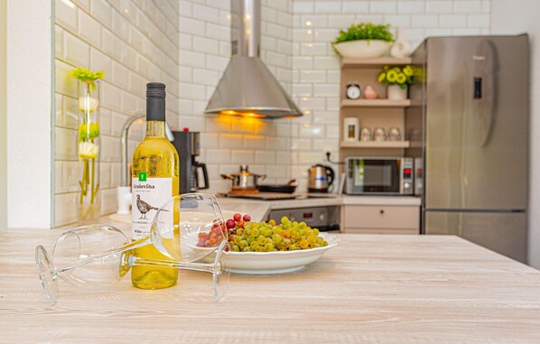 A kitchen with a bottle of wine, a bowl of grapes, and a wine glass on the counter.
