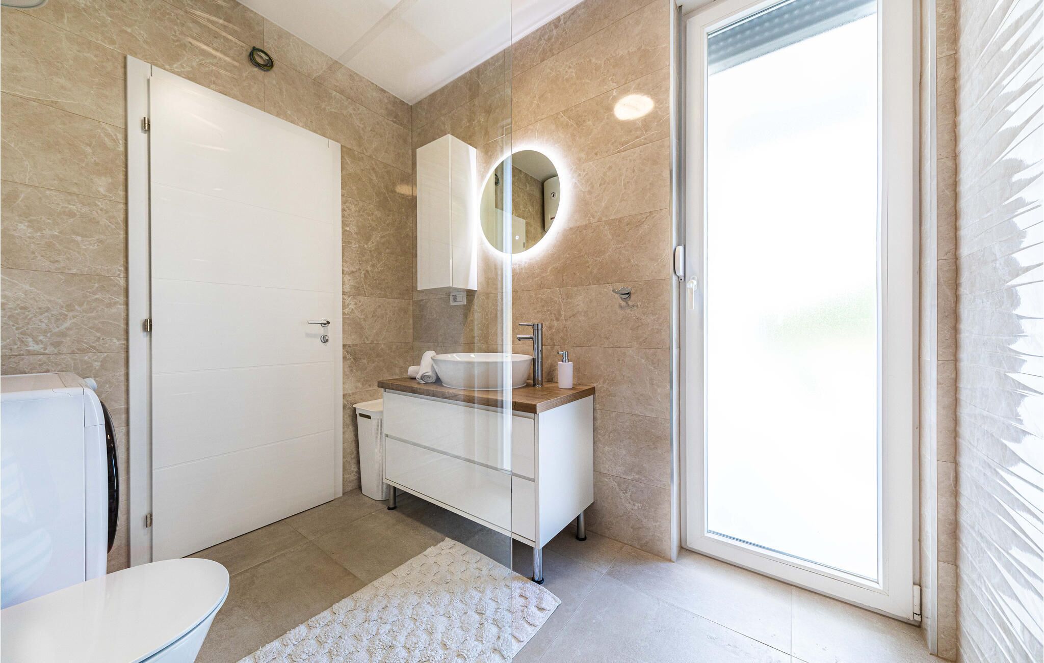 Une salle de bain moderne avec des toilettes blanches, un lavabo avec un miroir et une douche à parois de verre.
