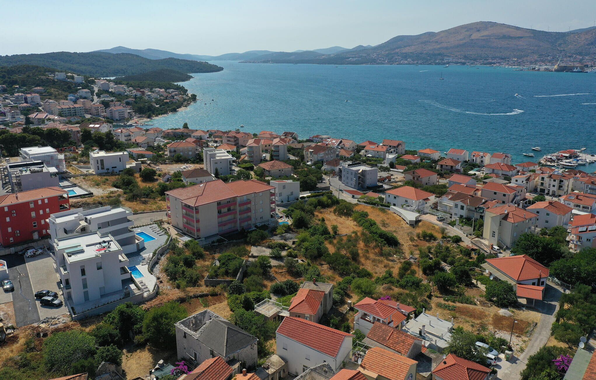 Vista aérea de una zona residencial costera con edificios, una piscina y vistas al mar.