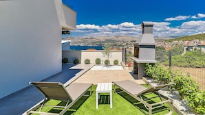 A rooftop patio with two lounge chairs, a small table, and a stone barbecue grill.