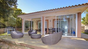 Eine moderne Terrassenanlage im Freien mit Korbmöbeln, einem Grill und einem Essbereich mit Tisch und Stühlen.