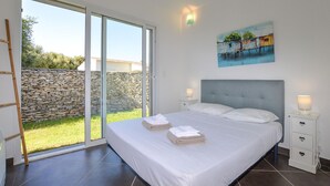 Ein Schlafzimmer mit einem großen Bett, zwei Nachttischen, einem Bild an der Wand und Blick auf eine Mauer aus Stein sowie auf Grünflächen außerhalb.