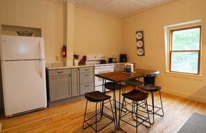 A kitchen with a refrigerator, stove, and bar stools.