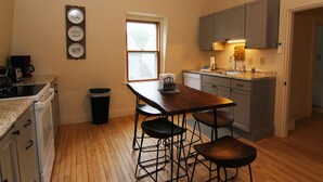 A kitchen with a wooden floor, a dining table with stools, a coffee maker, and a trash can.