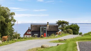 A house with a thatched roof, a red door, and a view of the sea. - Stunning home in Haderslev with sauna (Haderslev)