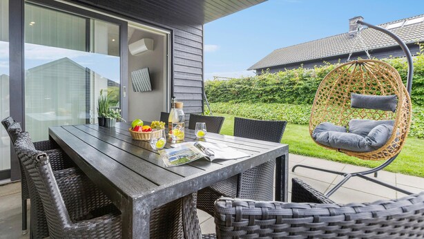 A modern outdoor dining area with a wooden table, wicker chairs, and a hanging chair. - Stunning home in Haderslev with sauna (Haderslev)
