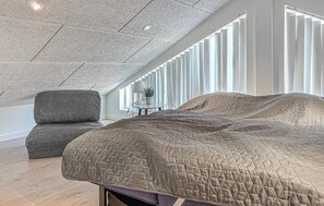 Una camera da letto moderna con un letto grande, una poltrona grigia e un soffitto con finestra a lucernario.
