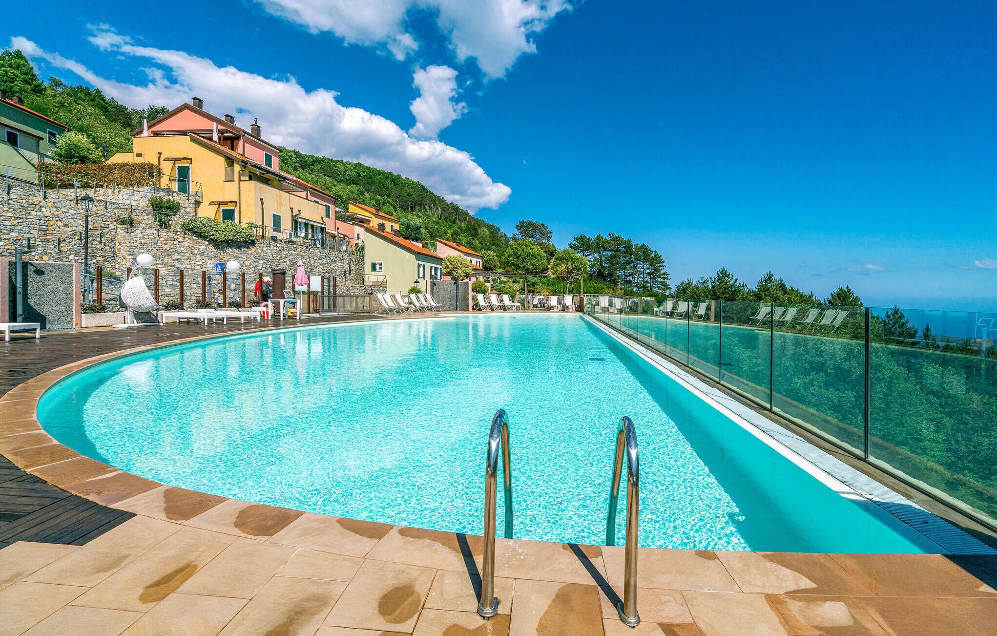 A large, clear swimming pool with a stone border, surrounded by lounge chairs and a stone wall.