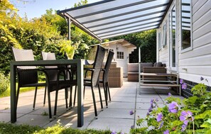 Une terrasse extérieure dotée d’un espace salon couvert, d’une table avec des chaises et d’un arrangement floral.