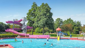 A swimming pool with multiple lanes, a water slide, and a playground area.