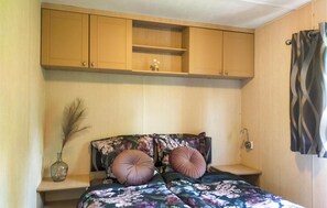 Une chambre à coucher avec un lit, des placards en bois au-dessus, une petite table et un vase contenant des plantes séchées.