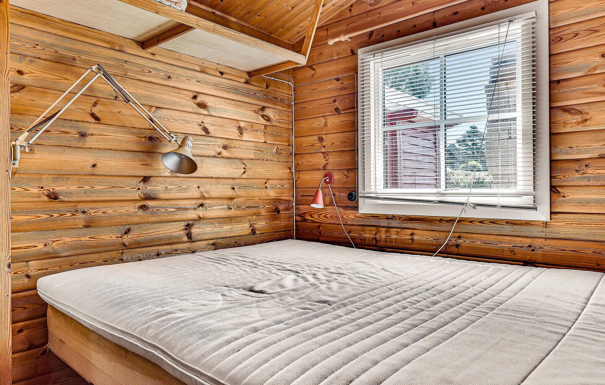 A wooden cabin room with a bed, a window with blinds, and a hanging lamp.