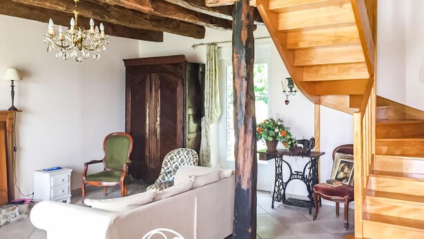 Un salón acogedor con una escalera de madera, un sillón verde, un sofá y una araña.