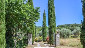 A pathway leading through a garden with tall cypress trees and a stone gate. - Cozy home in Cortona with kitchen (Cortona)