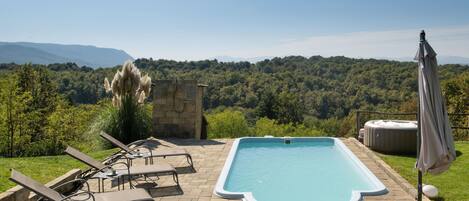 A rectangular pool with a stone surround, lounge chairs, and an umbrella.