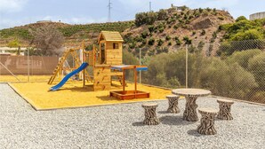 Un parque infantil con tobogán, estructuras para escalar y una casita de madera.