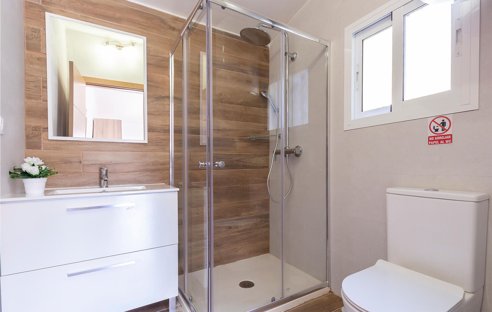 Une salle de bain moderne dotée d’une douche à parois de verre, d’un meuble-lavabo en bois, de toilettes et d’un miroir orné d’un motif en bois.