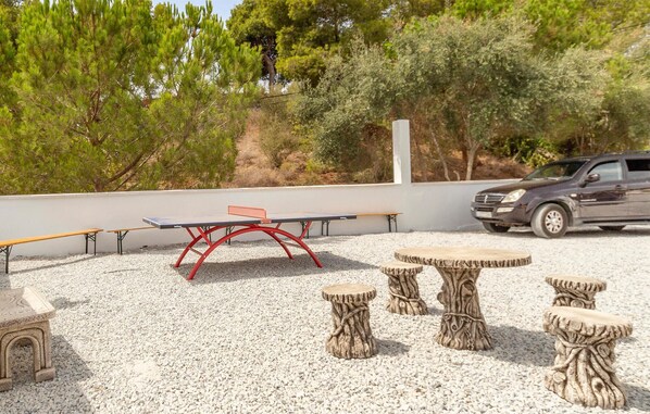 Un espacio al aire libre con una mesa de ping pong, bancos y taburetes hechos con tocónes de árbol.
