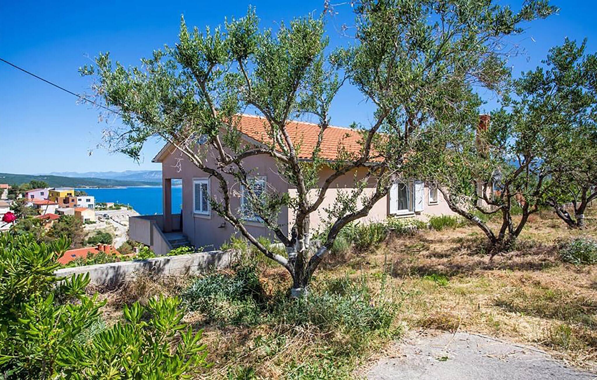 Une maison avec un toit recouvert de tuiles rouges, entourée de verdure et offrant une vue dégagée sur la mer.
