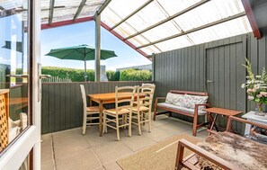 A covered patio with a wooden table and chairs, a bench, and a small table with a vase of flowers. - 1 bedroom amazing home in Stege (Stege)