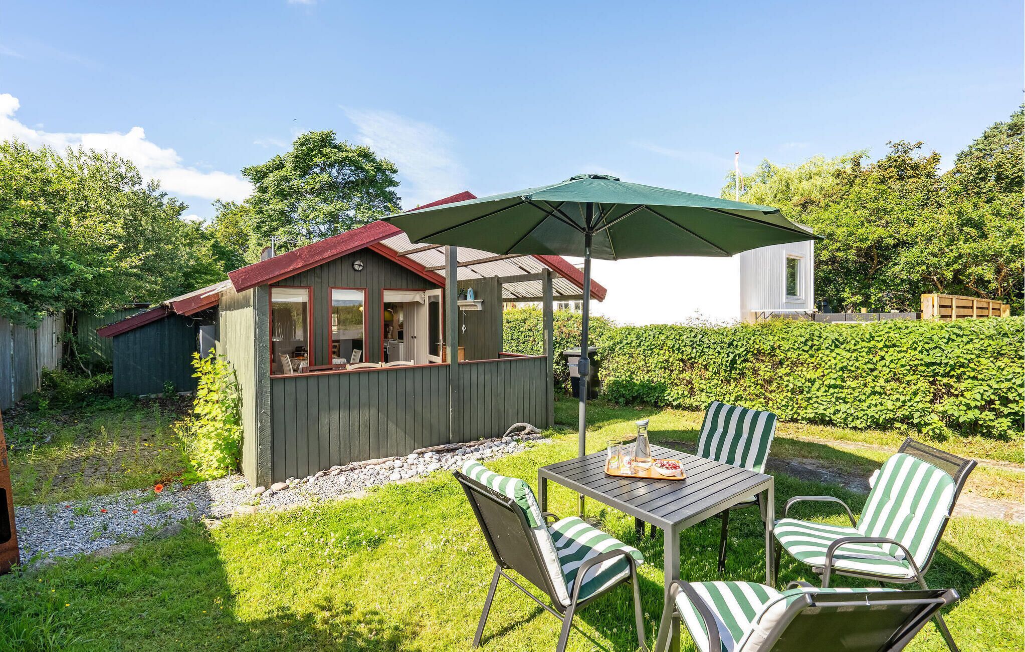 Ein Garten mit einem Holzschuppen, einem Tisch mit Stühlen und einem grünen Sonnenschirm.