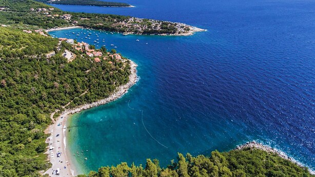 Eine Luftaufnahme einer Küstenregion mit Strand, Booten und einer kleinen Insel mit Gebäuden.