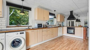 A modern kitchen with wooden cabinets, a built-in washing machine, and a large window with a view of greenery.