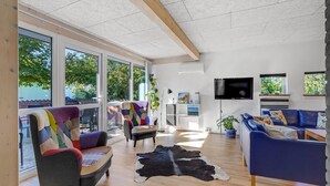 A spacious living room with large windows, a flat-screen TV, and a blue sofa.