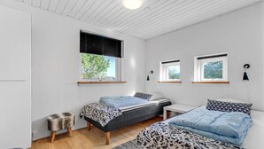 A bedroom with two beds, a small table, a bench, and three windows.