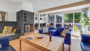 A modern living room with a fireplace, blue leather sofas, a wooden coffee table, and large windows offering a view of the outdoors.