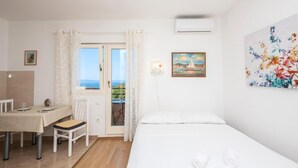 Ein Hotelzimmer mit einem Bett, einem Schreibtisch mit Stuhl, einem Vorhangfenster, einem Gemälde und einer Klimaanlage.