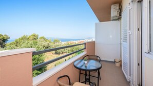 Ein Balkon mit Blick auf das Meer, ein kleiner Tisch mit einer Pflanze und ein weißer Kühlschrank.
