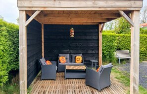 Een overdekt terras met rieten meubels en een houten vloer.
