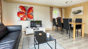 Un salon moderne comprenant un canapé, une table basse, un téléviseur et un coin repas avec des chaises et une table.