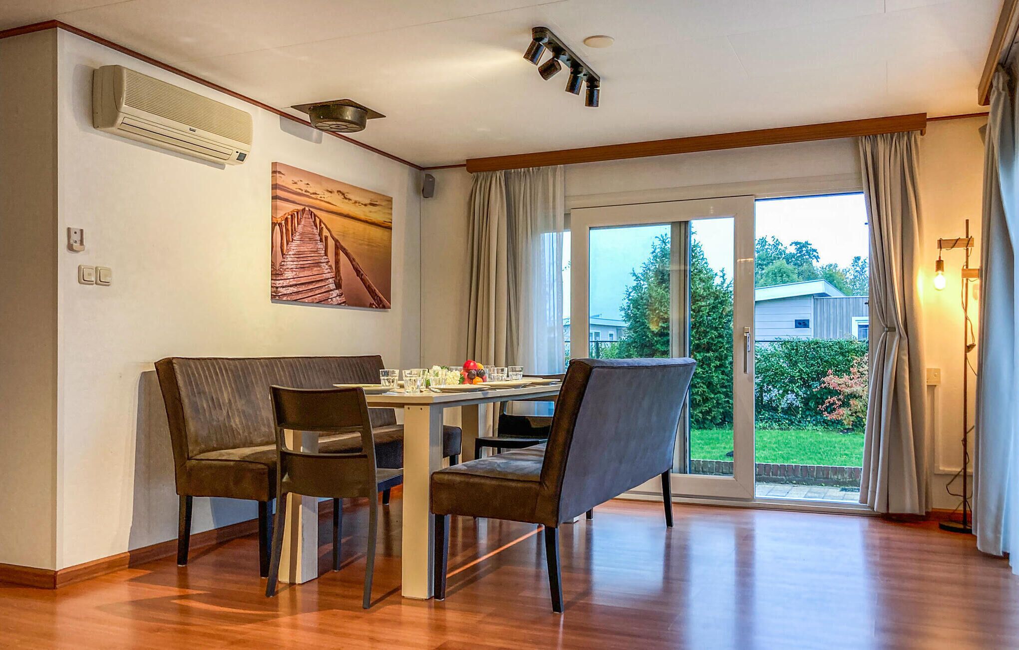 A dining area with a table and chairs, a painting on the wall, and a view through the glass door.