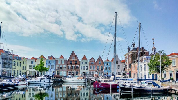 Un port de plaisance où sont amarrés des bateaux, entouré de bâtiments historiques aux toits recouverts de tuiles rouges.