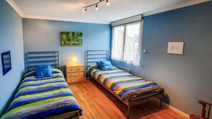 Une chambre avec deux lits simples, une table de chevet avec une lampe, une fenêtre avec des rideaux et un tableau au mur.