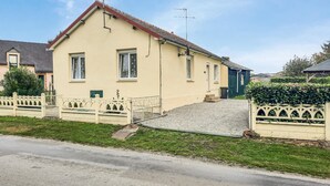 Une maison à deux étages, avec un toit en pente, un porche à l’avant et un petit jardin devant.