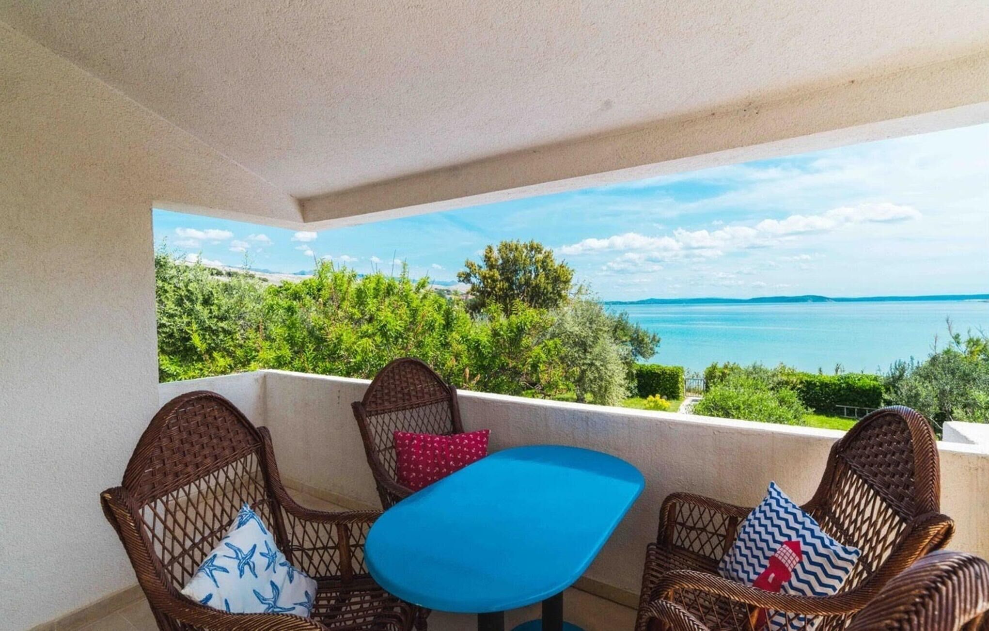 A balcony with wicker chairs and a small table, overlooking a scenic view of a body of water and greenery.