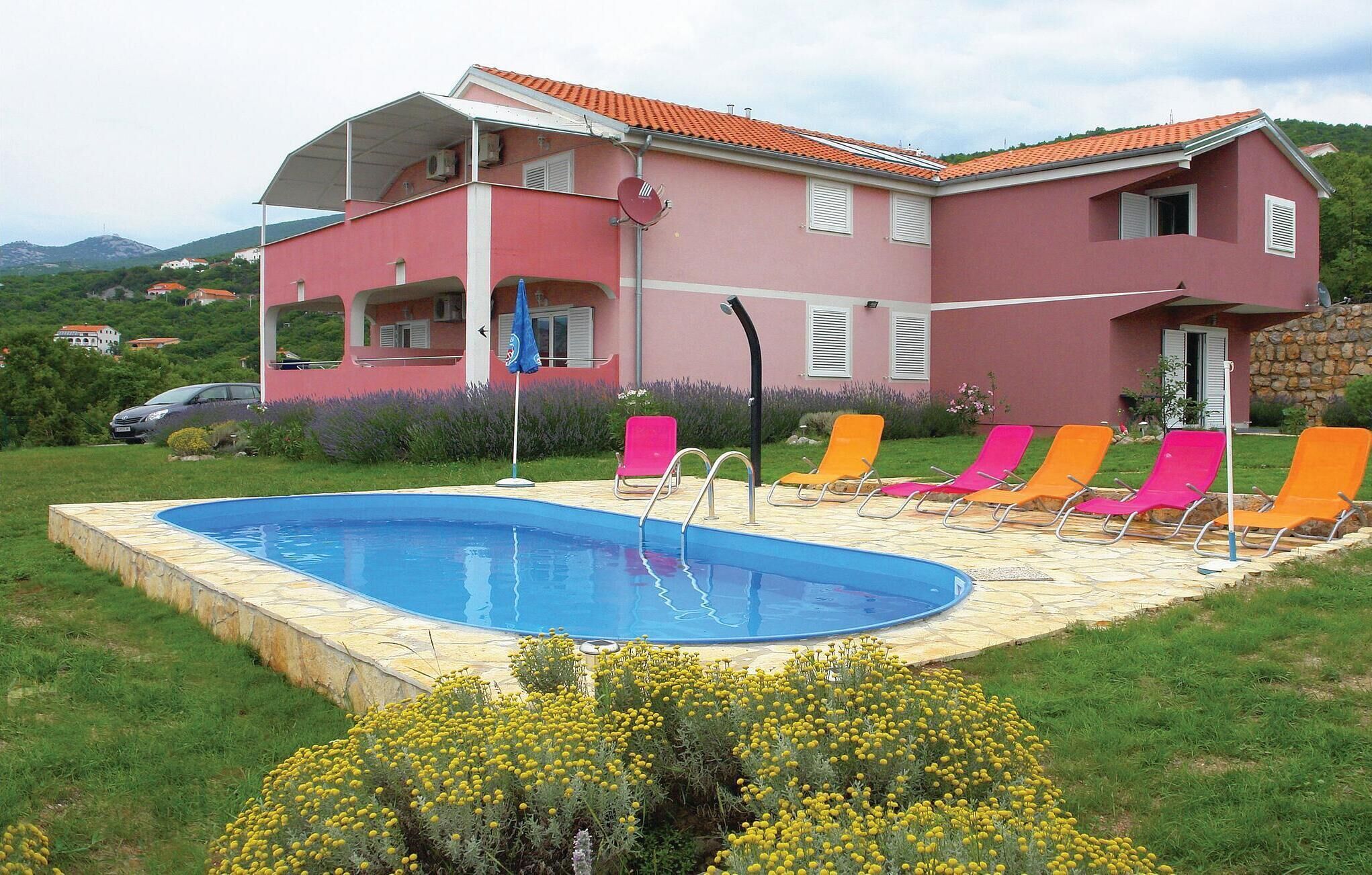 A two-story building with a swimming pool and multiple lounge chairs.