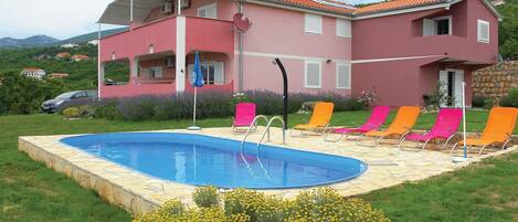 A two-story building with a swimming pool and multiple lounge chairs.