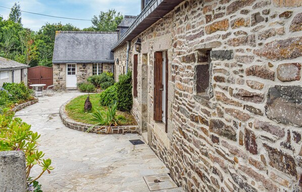 A stone building with a narrow courtyard, a wooden door, and a small garden area with plants and a table. - 6 bedroom awesome home in Plouézec (Plouezec)