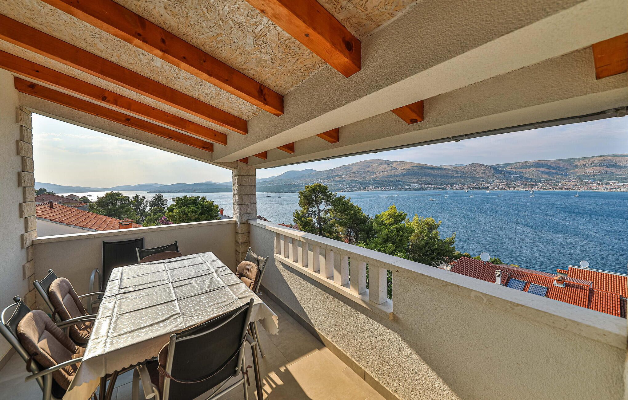 Un balcón con mesa y sillas, con vista a una masa de agua con barcos y un horizonte urbano distante.