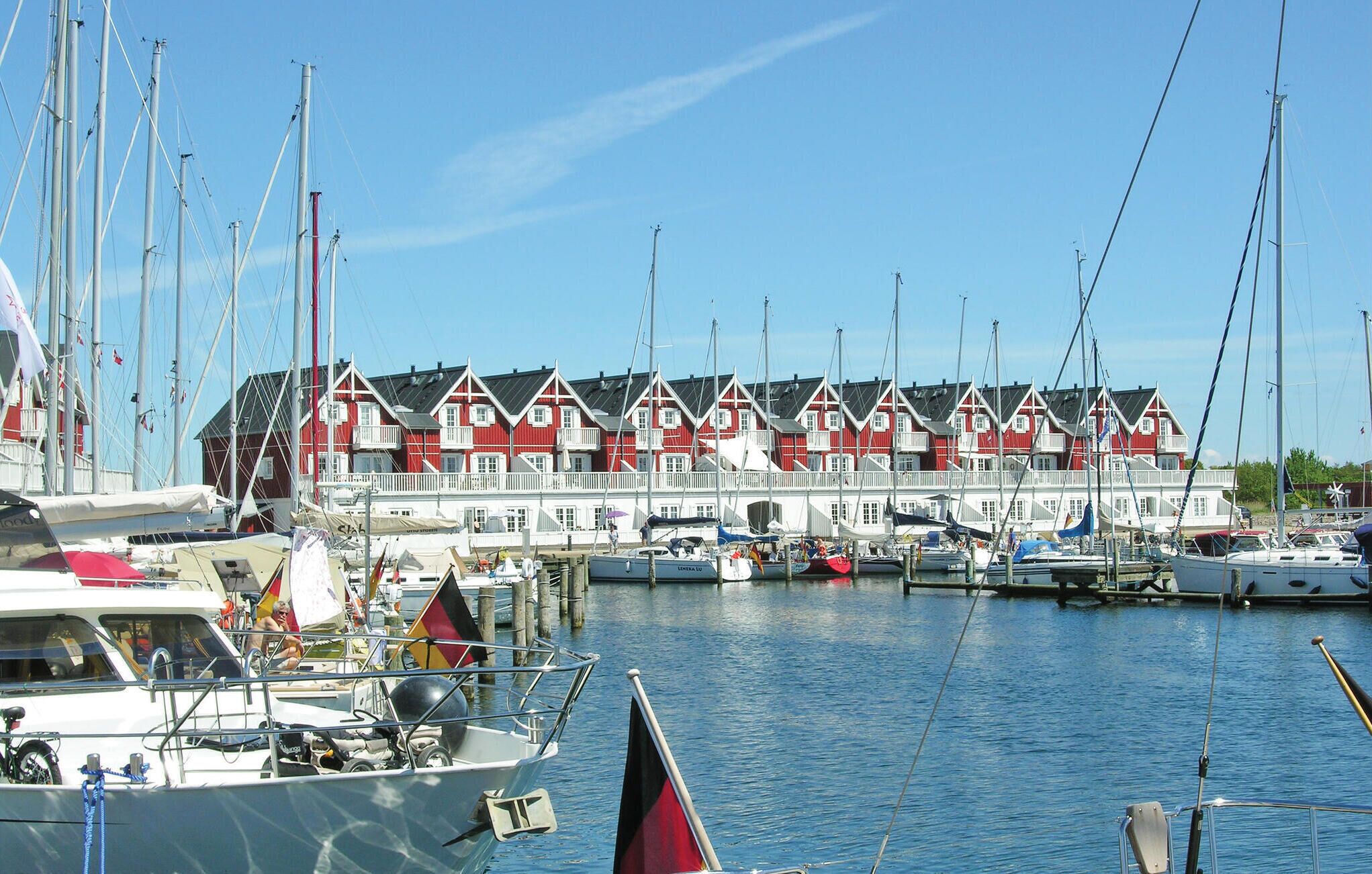 Uma marina com vários barcos atracados, uma fileira de edifícios vermelhos e brancos e céus azuis e límpidos.