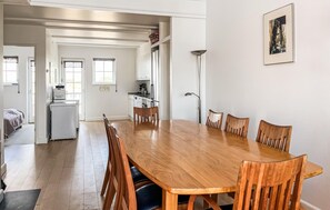 A spacious dining area with a wooden table and chairs, a kitchen in the background, and a framed picture on the wall.