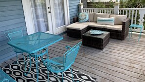 A covered outdoor patio with a blue metal table and chairs, a wicker sofa with cushions, and a patterned rug. - The Painted Lady, a spacious renovated 4BR Victorian (St. Augustine)